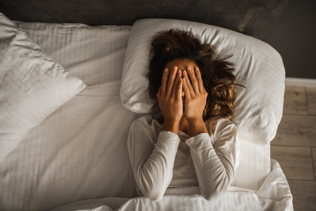 Mujer con expresión de fatiga en la cama, reflejando el sueño femenino fragmentado y menos reparador