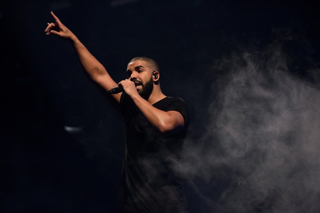 Drake en concierto con fondo de luces azules celebrando su récord de 14 No. 1 en Billboard