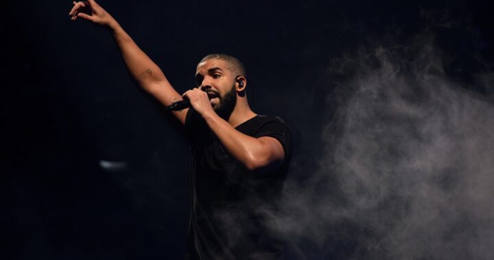 Drake en concierto con fondo de luces azules celebrando su récord de 14 No. 1 en Billboard