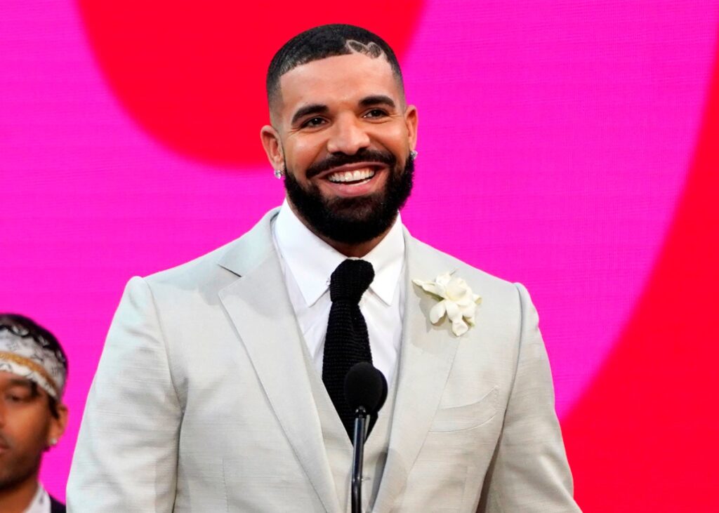Drake sonriendo en una imagen de archivo con un fondo de vinilos de discos, con una mano en el corazón