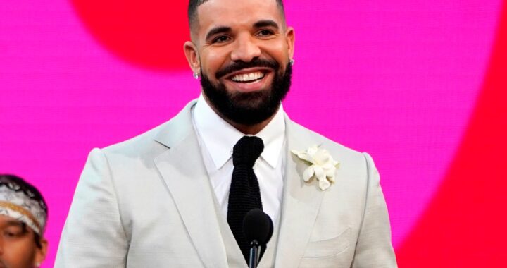 Drake sonriendo en una imagen de archivo con un fondo de vinilos de discos, con una mano en el corazón