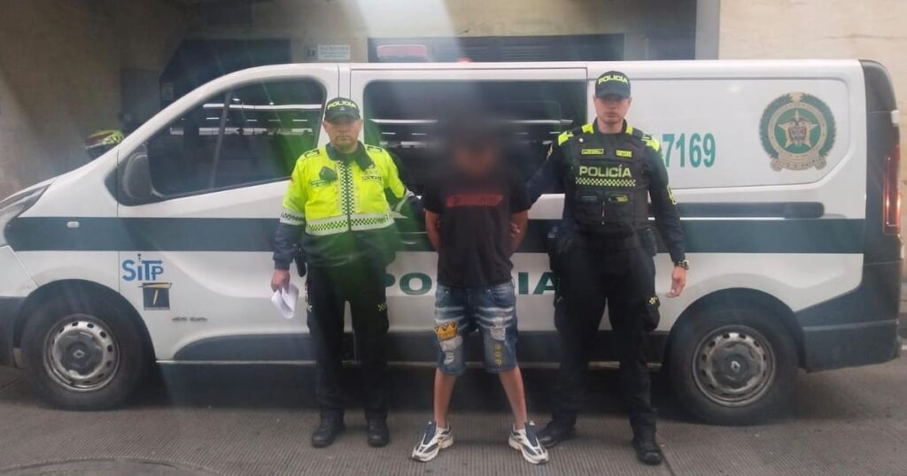 Imagen de un agente de policía realizando un arresto, con un hombre esposado al fondo