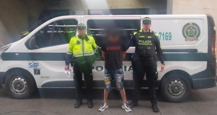 Imagen de un agente de policía realizando un arresto, con un hombre esposado al fondo