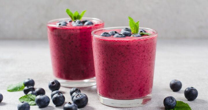 Una persona sosteniendo un vaso de agua con limón, rodeada de frutas cítricas y hierbas frescas