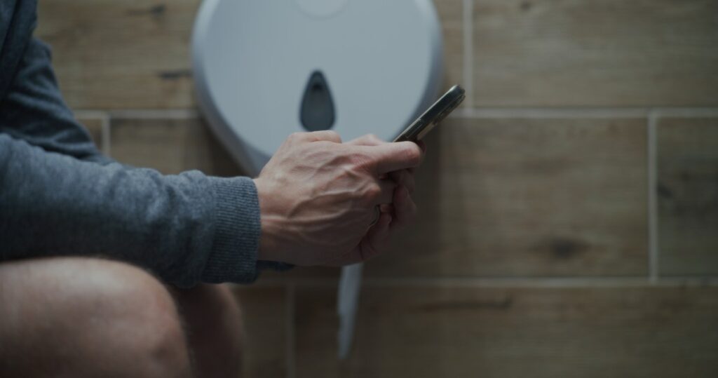 Persona sentada en el baño con el teléfono en la mano, con una expresión de alerta y preocupación