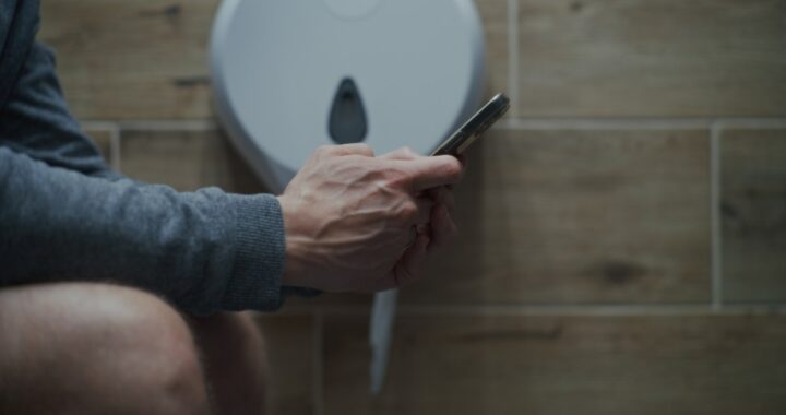 Persona sentada en el baño con el teléfono en la mano, con una expresión de alerta y preocupación