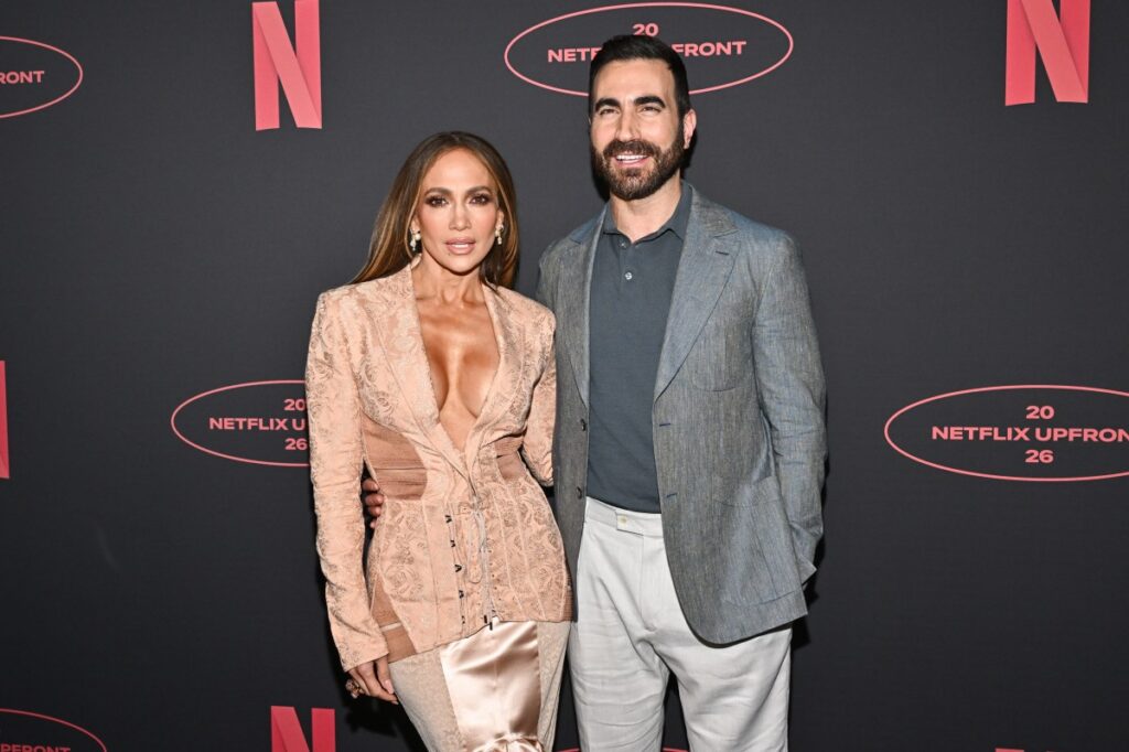 Jennifer Lopez y Brett Goldstein sonriendo en entrevista de 'Today' tras desmentir rumores de romance, con cartel de 'Office Romance' de fondo