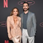 Jennifer Lopez y Brett Goldstein sonriendo en entrevista de 'Today' tras desmentir rumores de romance, con cartel de 'Office Romance' de fondo