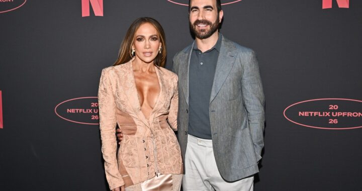 Jennifer Lopez y Brett Goldstein sonriendo en entrevista de 'Today' tras desmentir rumores de romance, con cartel de 'Office Romance' de fondo