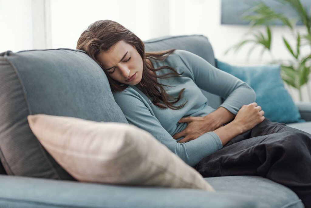 Mujer con expresión de dolor abdominal intenso sosteniendo un reloj de arena, simbolizando la espera por atención médica