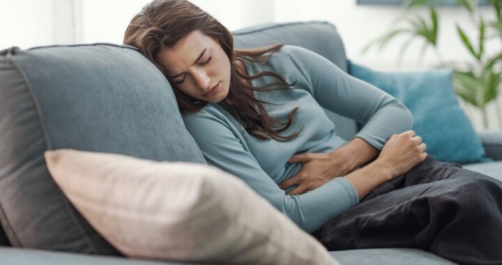 Mujer con expresión de dolor abdominal intenso sosteniendo un reloj de arena, simbolizando la espera por atención médica